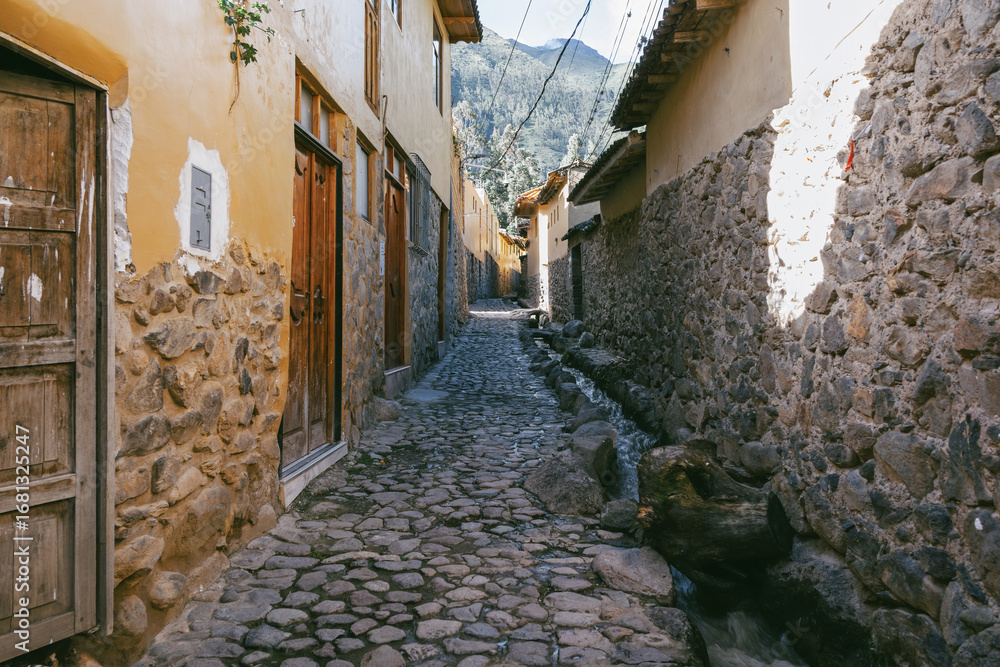 Obraz premium Traditional narrow alleyway with ancient Inca stone walls and cobblestone pavement in the historic town of Ollantaytambo, Peru.