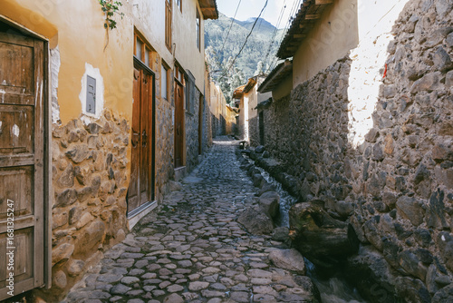 Traditional narrow alleyway with ancient Inca stone walls and cobblestone pavement in the historic town of Ollantaytambo, Peru.