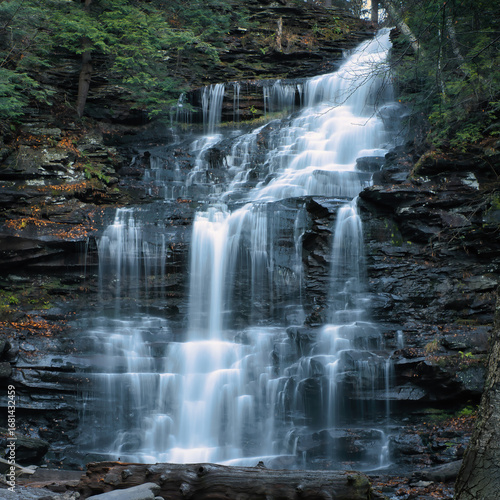 Silky cascading waterfall flowing over layered rock formations with autumn leaves