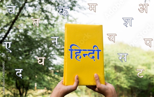 Hindi text written with hand holding Hindi book in green garden background.