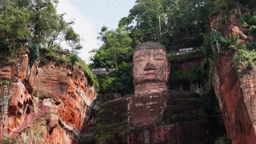 Detailed slow motion view of full Leshan Buddha carved in red sandstone with textures of surrounding natural cliff face