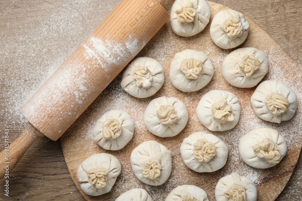 Fototapeta premium Uncooked khinkalis (dumplings) and rolling pin on wooden table, top view