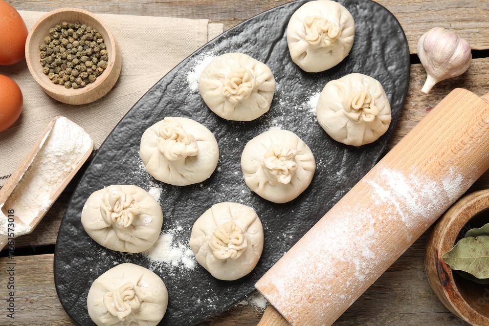 Fototapeta premium Uncooked khinkalis (dumplings), flour, spices, eggs and rolling pin on wooden table, flat lay
