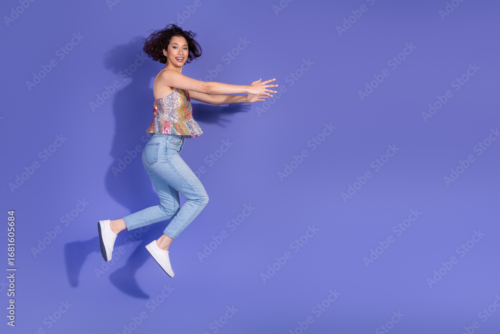 Fototapeta premium Smiling young woman in casual fashion jumping on a vibrant purple background showcasing joy and positivity