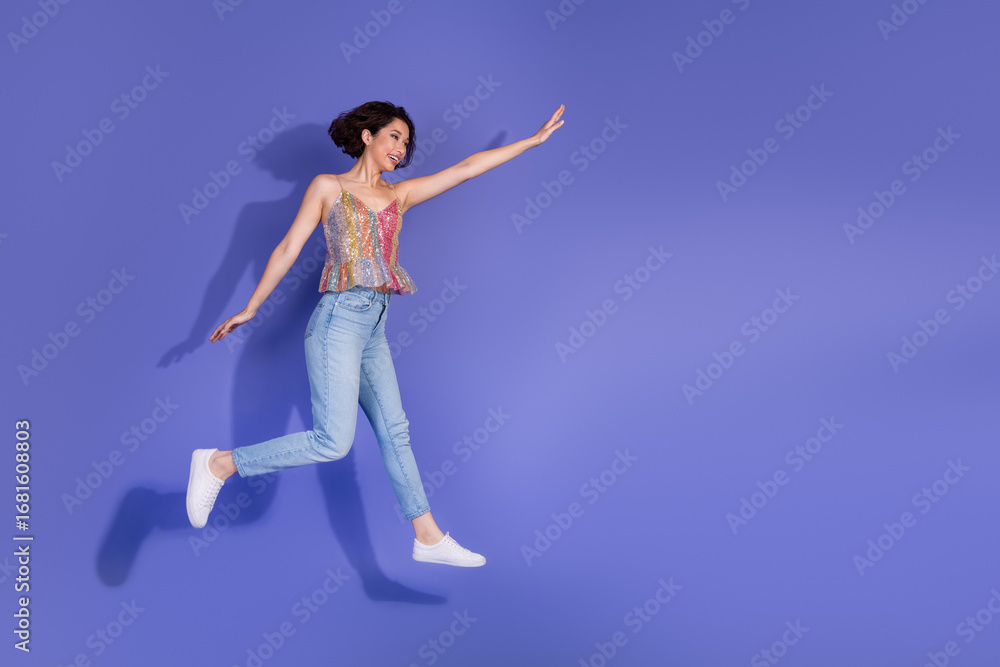 Obraz premium Funky stylish woman in casual fashion jumping joyfully against a purple background in a shiny sequined top and jeans