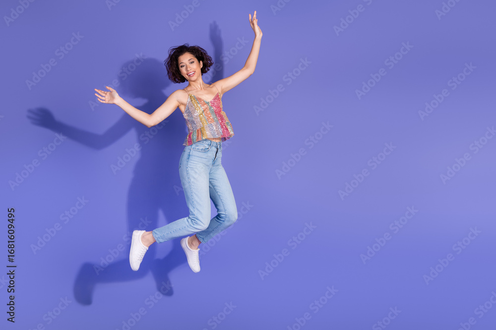 Obraz premium Cheerful female in casual denim and sequined top joyfully jumping against a purple background emphasizing vibrant energy