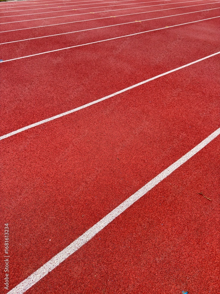 Fototapeta premium Vibrant red athletic track with white lane lines offering a dynamic perspective for sports and competition concepts.