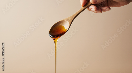Wooden spoon drizzling honey on a cream background sweet golden minimal food drip concept
