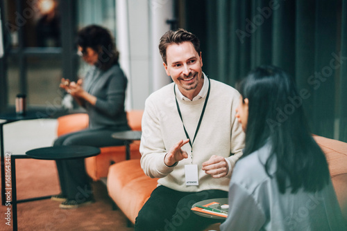 Smiling businessman communicating with colleague while sitting at networking event in convention center
