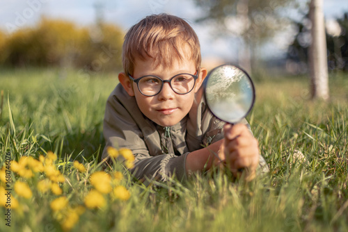 Boy exploring nature. Scout club and outdoor science activities. Boy wayching plants with magnifying glass. Child exploring environment.