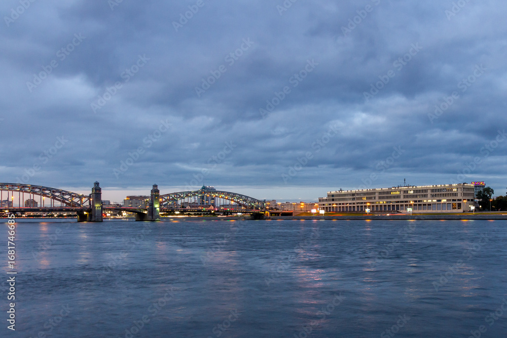 Naklejka premium Dusk view of illuminated Bolsheokhtinsky Bridge over Neva River with city lights reflection in water. Saint Petersburg, Russia.