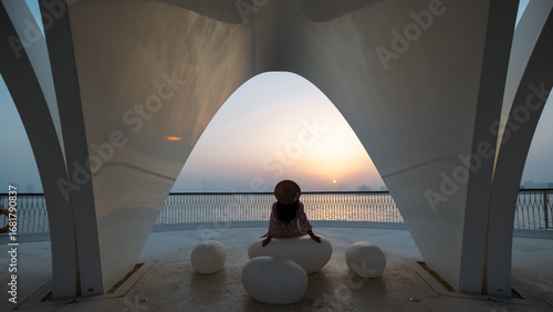 Sunset at Dubai creek harbour with silhouette of a girl sitting by waterfront wearing a hat and flowy dress, cinematic fashion photography in Dubai