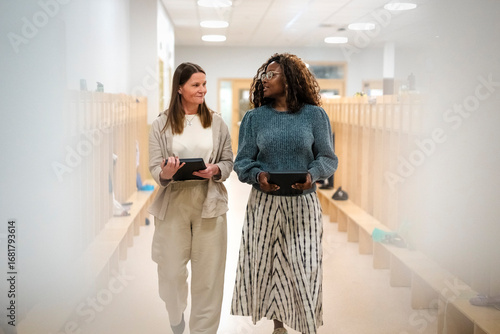Multiracial female teachers talking with each other while walking in corridor at elementary school