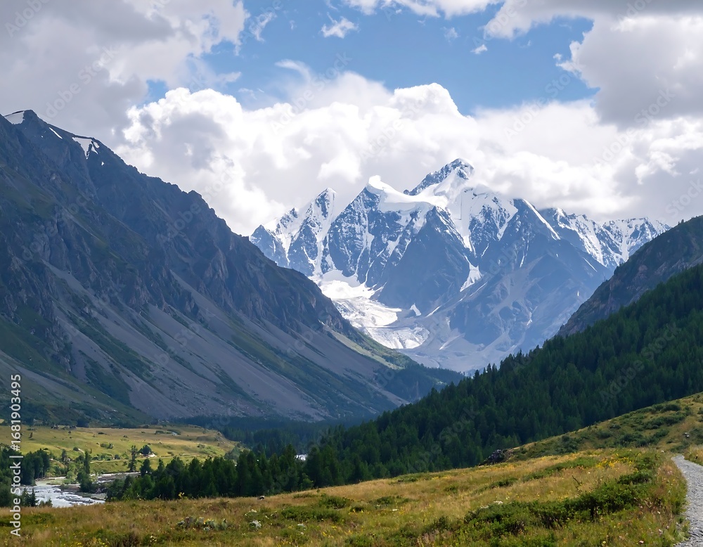 Naklejka premium Majestic snow-capped mountains rise above a valley carpeted in green forests and grasslands, showcasing a breathtaking landscape.