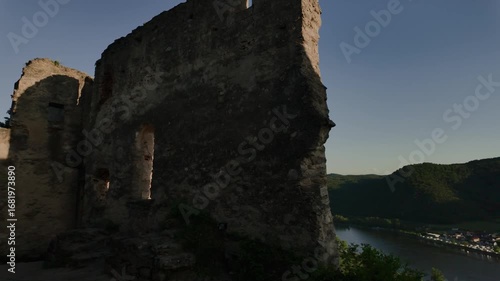 Video moving from medieval castle ruins to a scenic panorama of Dürnstein town, green hills and vineyard valleys in Austria’s Wachau region. Historic and picturesque view.