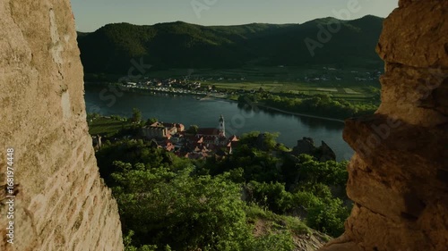 Video moving forward through medieval ruins to reveal Dürnstein town, its central cathedral, cozy houses, vineyards, green hills and the Danube River in Austria.