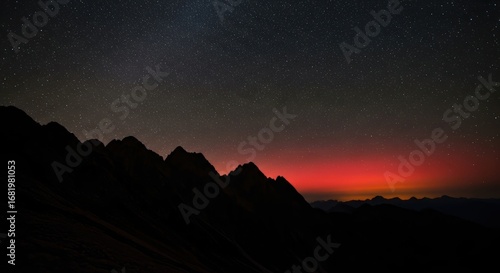 Starry night sky over mountain silhouette with vibrant sunset horizon