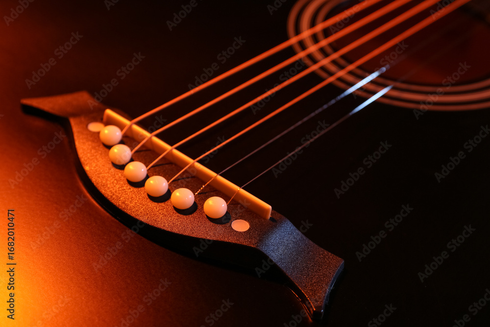 Fototapeta premium Modern black guitar with orange light as background, closeup