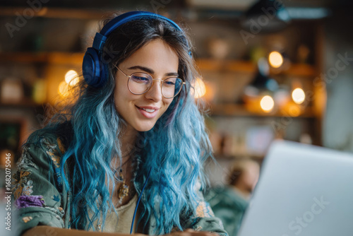 Smiling freelance girl with blue hair working on laptop in loft cafe with modern interior, concept of online work
