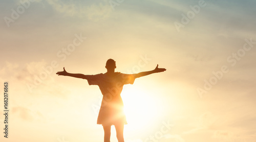 Vászonkép silhouette of a woman standing with open arms, embracing the warmth and light of