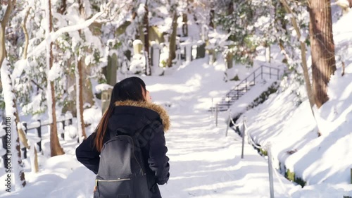Happy Asian woman traveler travel local village countryside covered in snow in Japan. Attractive girl enjoy outdoor lifestyle walking and looking beautiful nature pine tree forest in winter season.