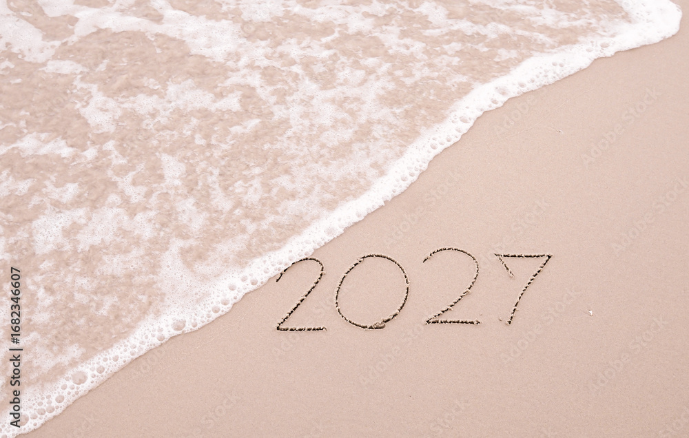 Fototapeta premium 2027 year handwritten with ocean waves on a sandy beach. New Year 2027 concept
