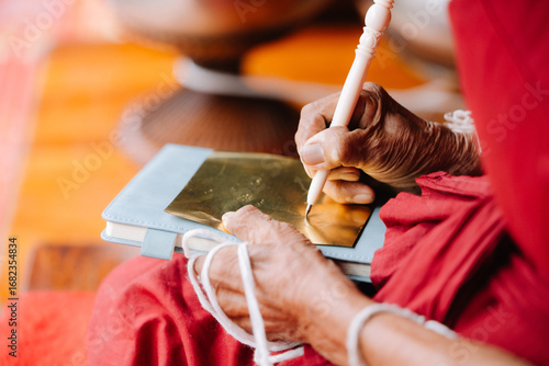 Wallpaper Mural An elderly person's hands hold a white thread, likely part of a Buddhist practice, with an orange robe in the background. Torontodigital.ca