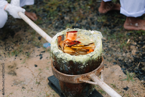 Wallpaper Mural A close-up shot of a crucible containing what appears to be molten metal, held by a long handle, suggesting a process of casting or smelting. Torontodigital.ca