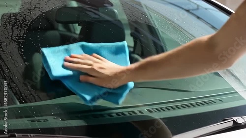 Man diligently cleaning car windshield with a blue microfiber cloth, showing clear visibility.