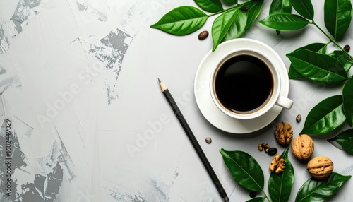 Dark coffee in a white cup with leaves, walnuts, and a pencil on a textured gray surface viewed from above
