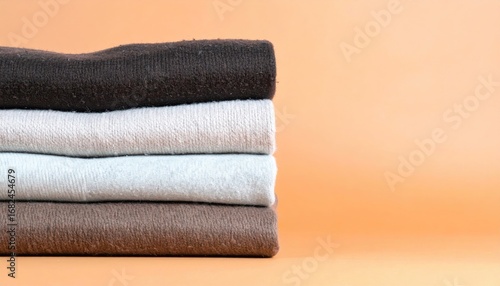 Neatly stacked folded shirts in neutral tones brown, white, and light blue, with an orange background. Soft focus