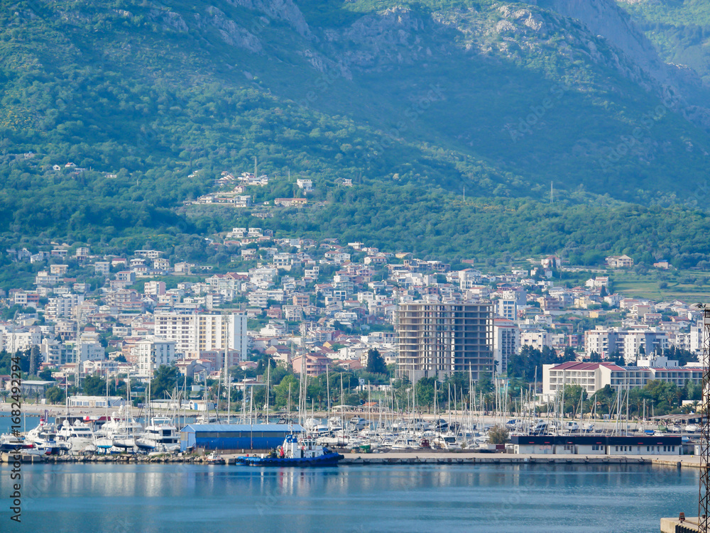 Fototapeta premium Scenic view of yacht club and marina in Bar, Montenegro, with boats, city buildings, and mountains in the background.