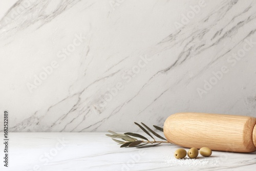 Wooden rolling pin and olives rest on marble