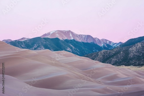 Pastel sunset hues illuminate sand dunes and snow-capped mountains