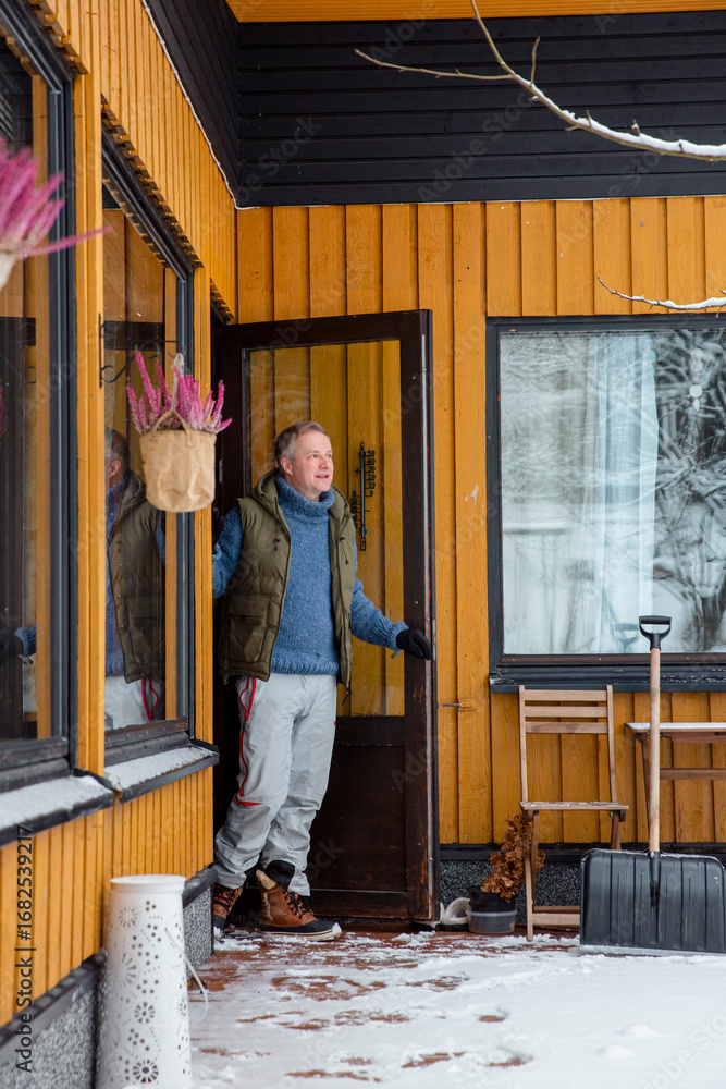 Fototapeta premium Middle-aged man stepping out into snowy yard to perform winter chores, outdoor lifestyle and seasonal activity, cold weather and active routine.