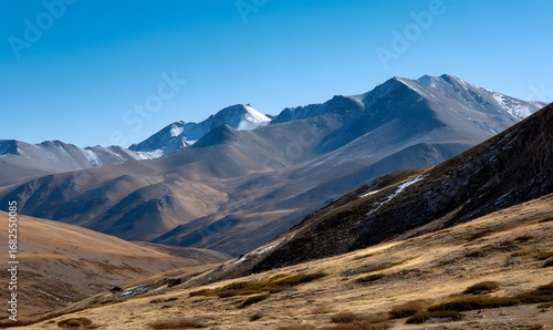 vast mountain range under clear blue sky, sunlit peaks with warm golden tones,