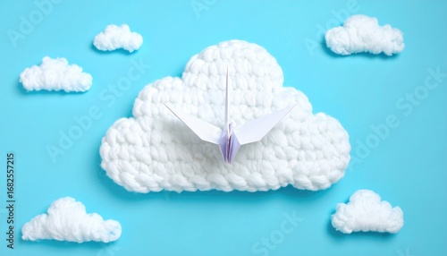 A paper origami bird soars from a fluffy, crocheted cloud surrounded by smaller clouds on a bright cyan background. Peaceful, simple, clean composition