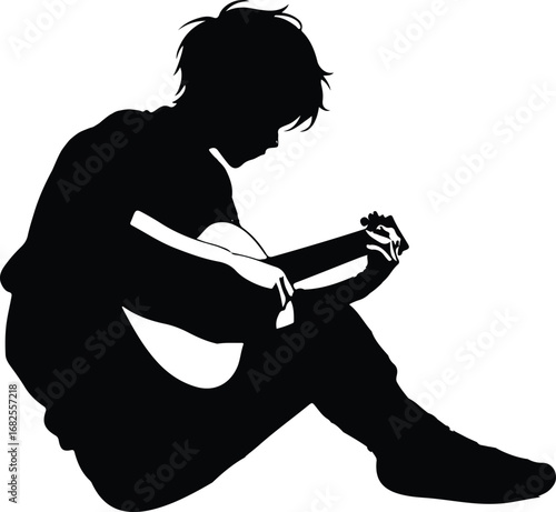 A black silhouette of a young person sitting cross-legged, deeply engrossed in playing an acoustic guitar, their head bowed in concentration.
