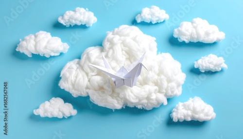 Origami crane rests on a fluffy cloud-like material amidst small puffy clouds, all on a soft blue background creating a dreamy, peaceful ambiance