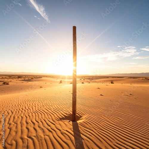 Solitary wooden post rising from rippled sand dunes, bathed in golden sunlight under a vast, clear sky. Desert landscape