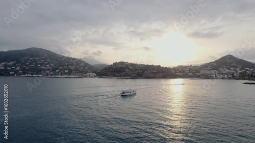 Under a soft sunset glow, a lone boat glides through the tranquil waters off Mandelieu La Napoule, surrounded by the picturesque landscape of the French Riviera, capturing serenity and wanderlust.