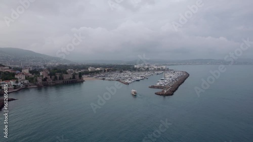 Gliding into Mandelieu La Napoule, aerial drone footage captures the majestic marina filled with yachts against a lush, coastal backdrop. Misty skies enhance the timeless charm of the South of France