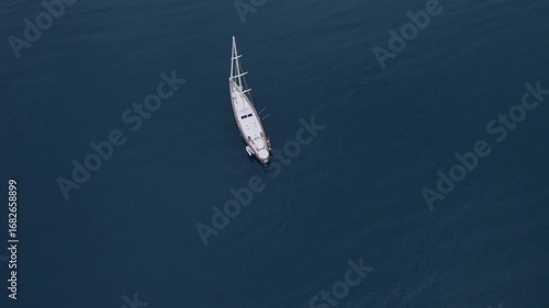 Aerial drone footage of a solitary sailing boat navigating through the vast, calm waters of the South of France under a serene sky. The scene emphasizes the tranquility and freedom of open sea travel