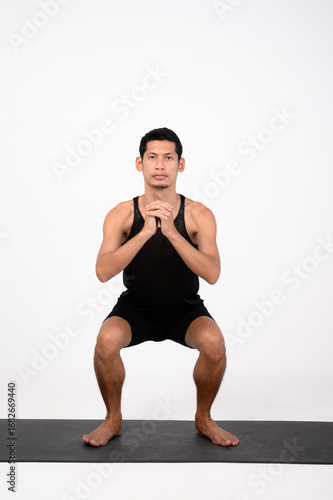 Font view bodyweight squat . A male runner performs a bodyweight squat on a fitness mat, clasping his hands in front of his chest.