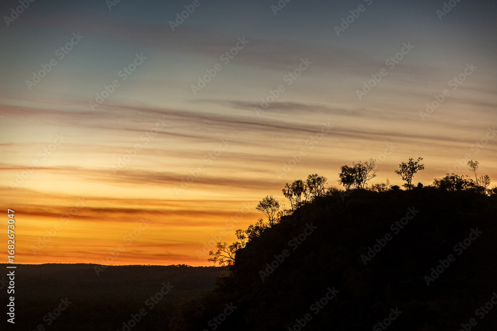 Obraz premium Sunset with a mountain and silhouetted trees.