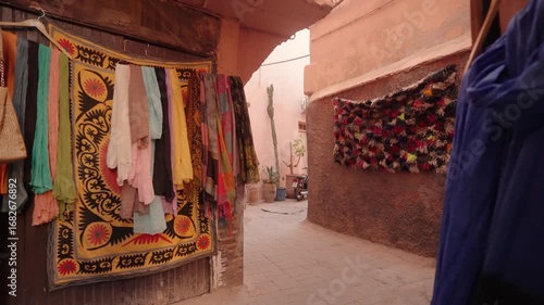 Brightly colored scarves and fabrics hang on display inside a Moroccan market alley.