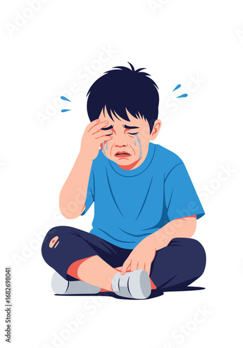An asian child sits cross-legged crying with his hand covering his eyes and tears streaming down his face illustrating emotional distress and sadness