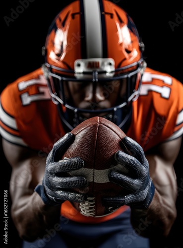 A football player in an orange uniform is holding a football