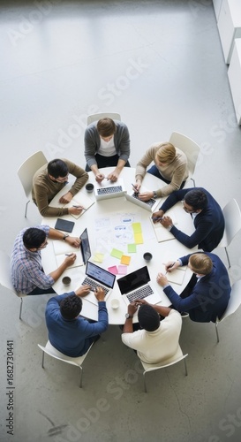 Diverse group of people collaborating around a white table with laptops and notes business meeting collaboration