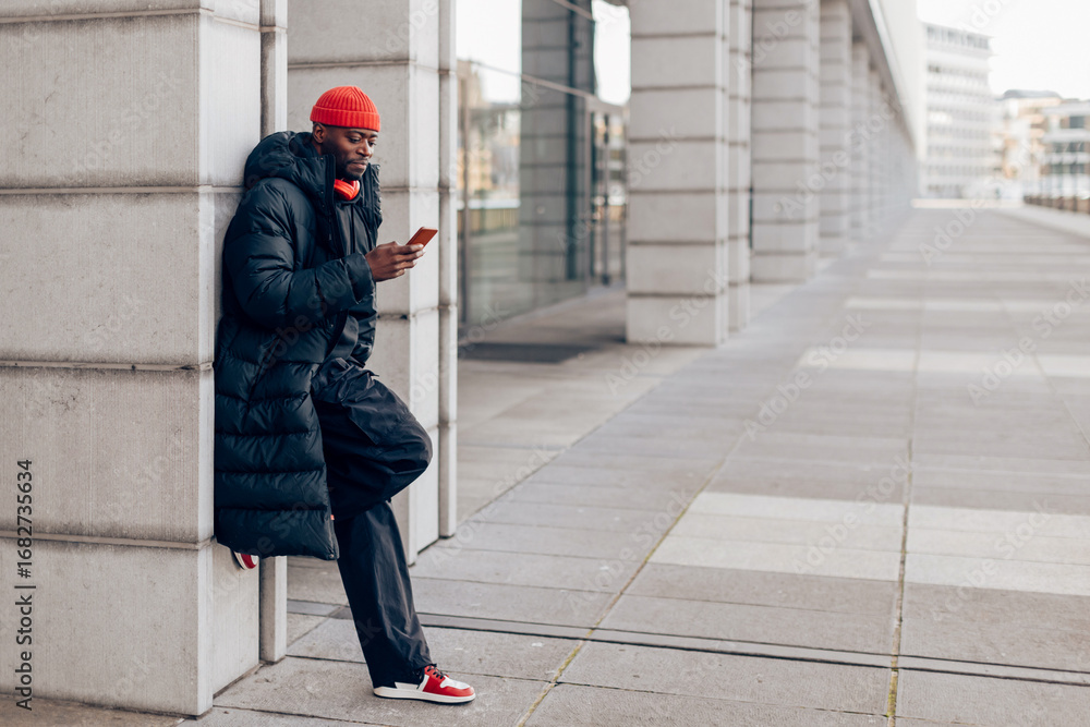 Fototapeta premium Stylish man using smartphone while leaning against column in the city